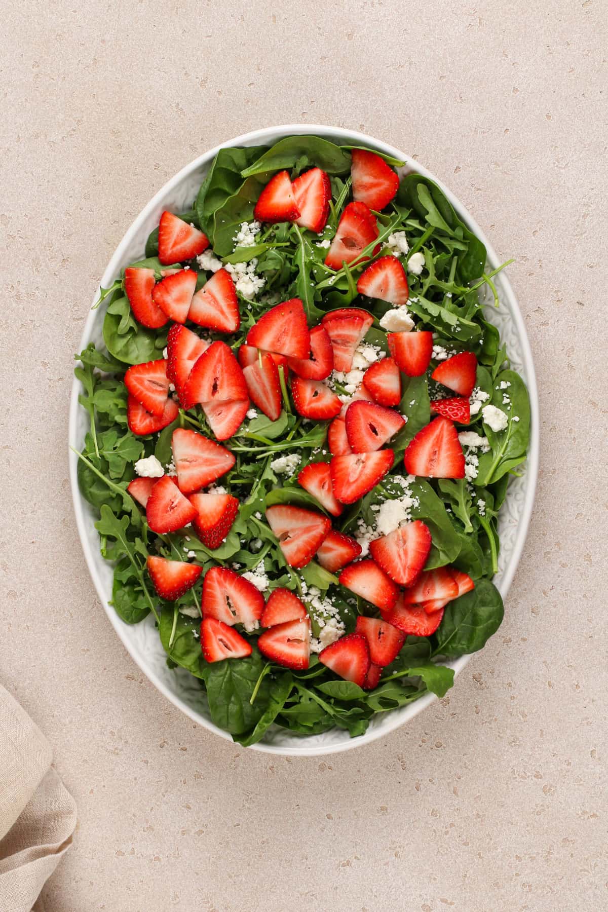 Greens topped with goat cheese and strawberries in a serving bowl.