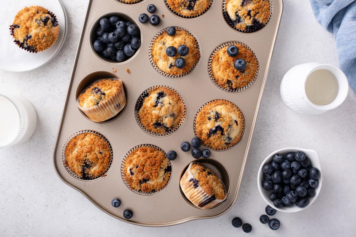 Overhead view of cooled bisquick blueberry muffins arranged with fresh blueberries in a muffin tin.