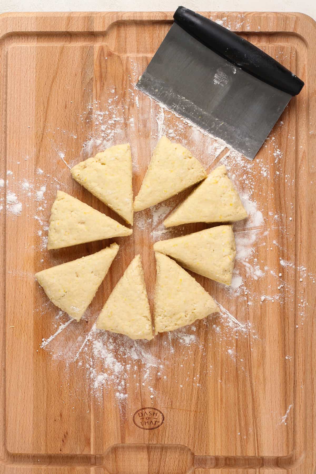 Lemon scone dough cut into triangles on a wooden board.