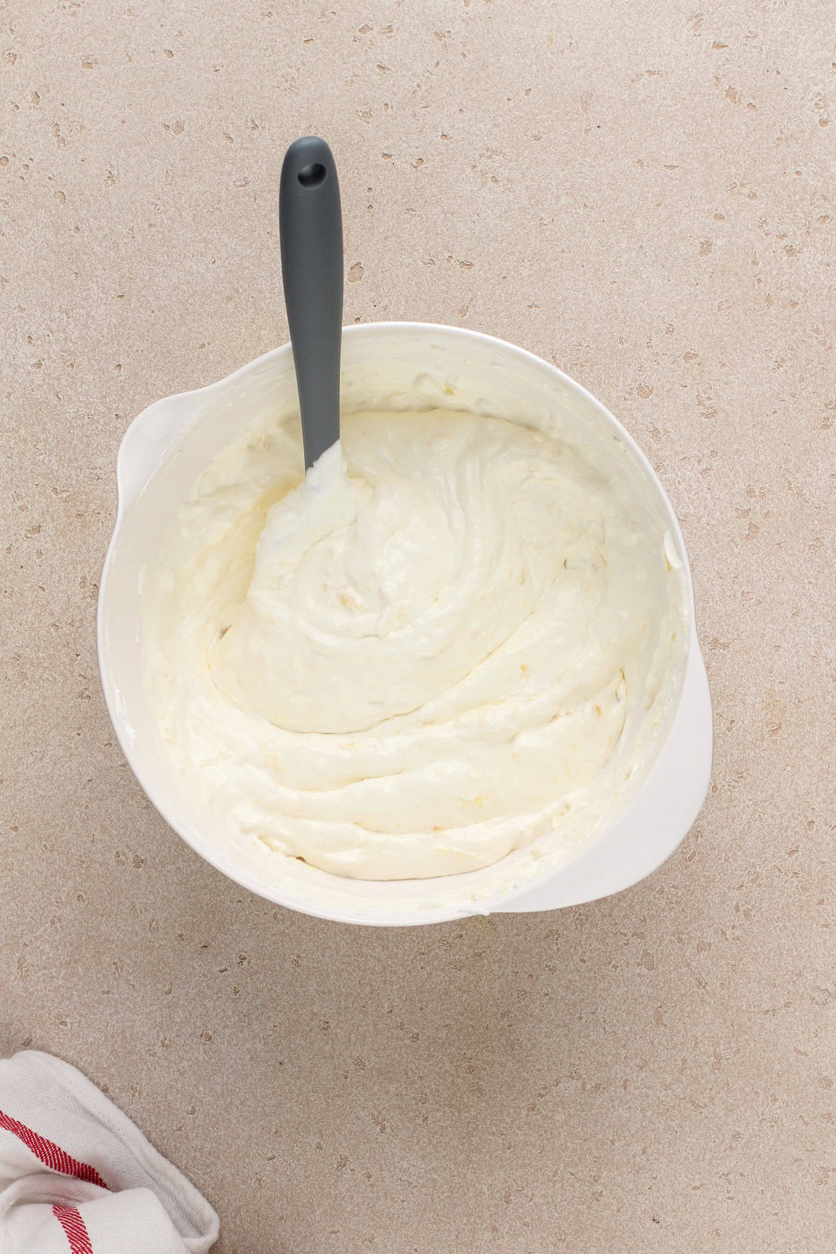 Frosting for easy pineapple cake mixed together in a white bowl.