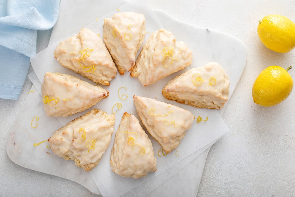 Overhead view of glazed lemon scones arranged in a circle on a piece of parchment paper over a marble board.