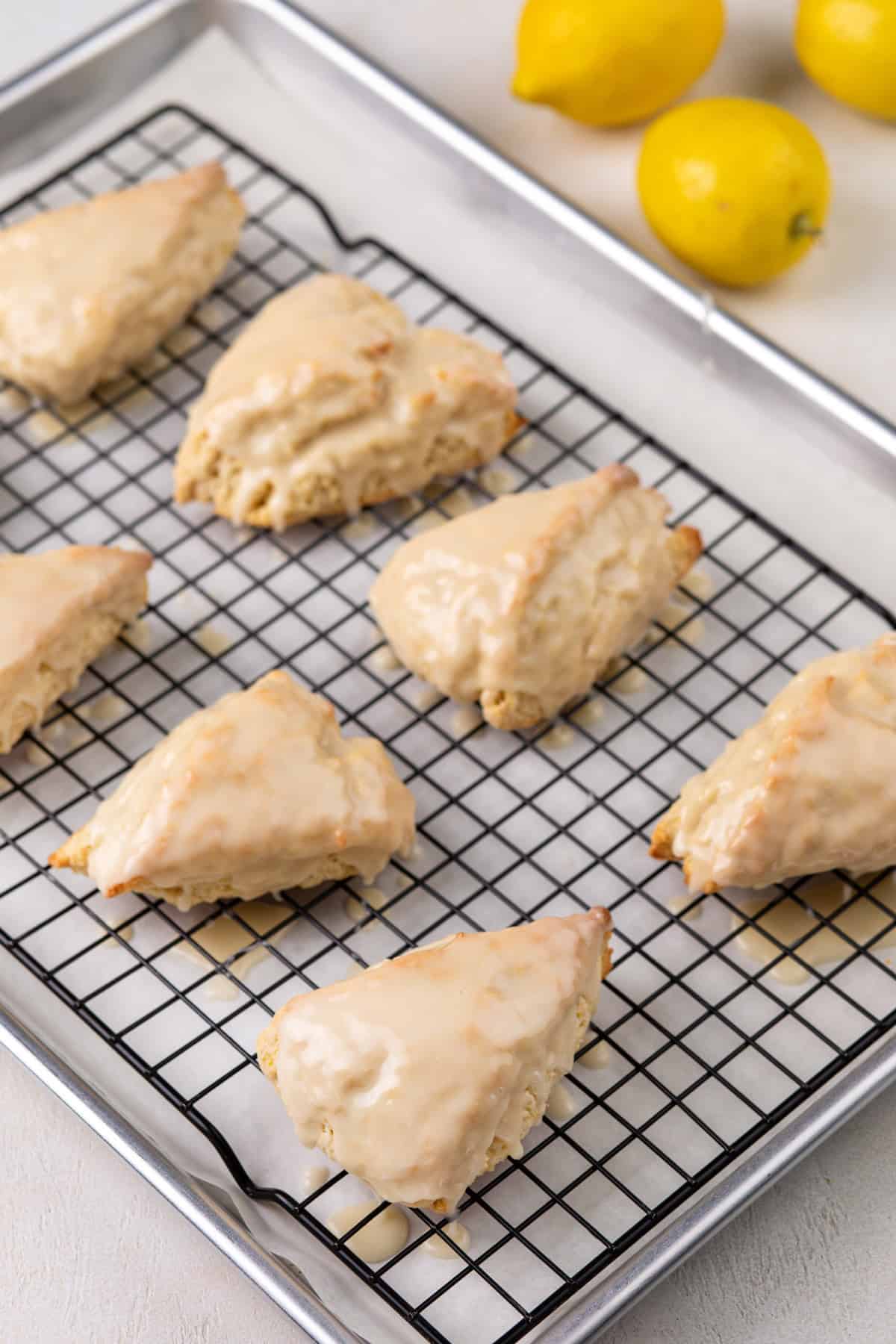 Freshly glazed lemon scones on a wire rack over a sheet pan.