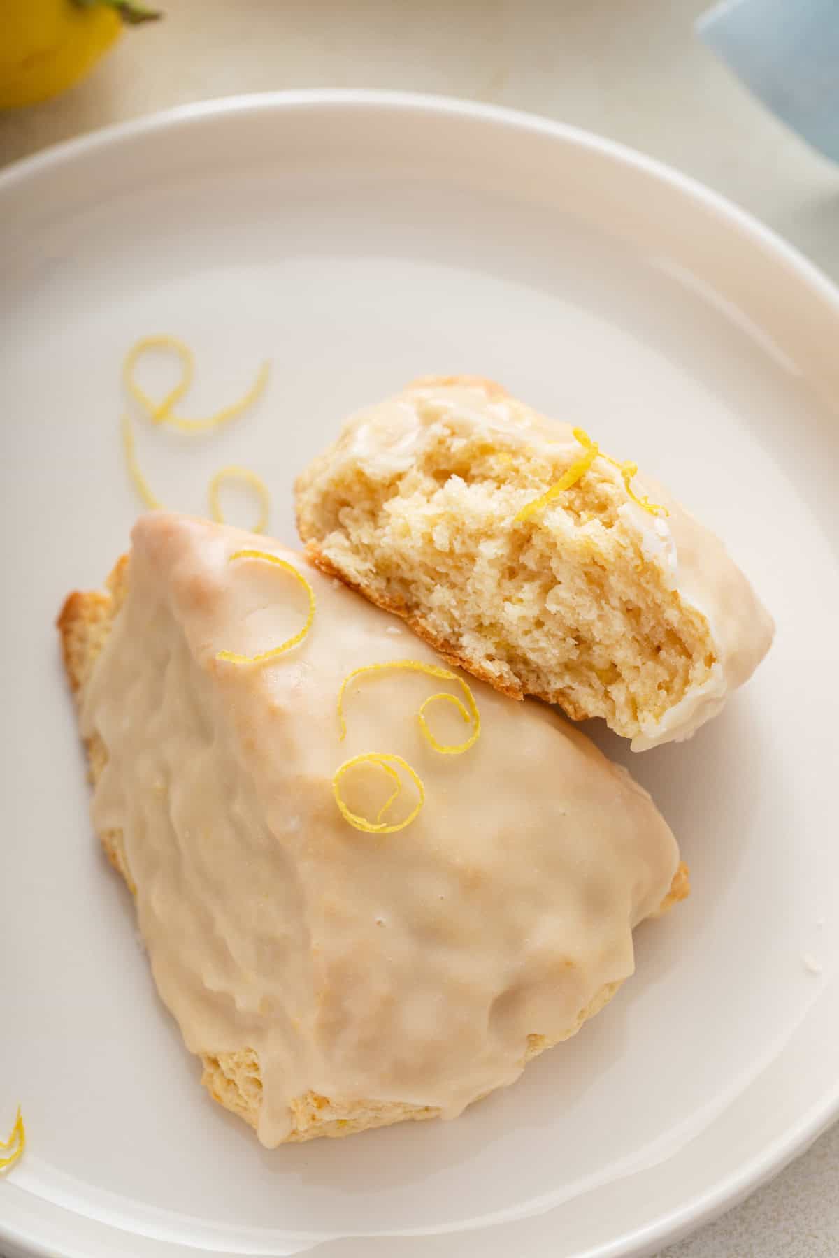 Halved lemon scone propped against a second scone on a white plate to show the tender crumb.