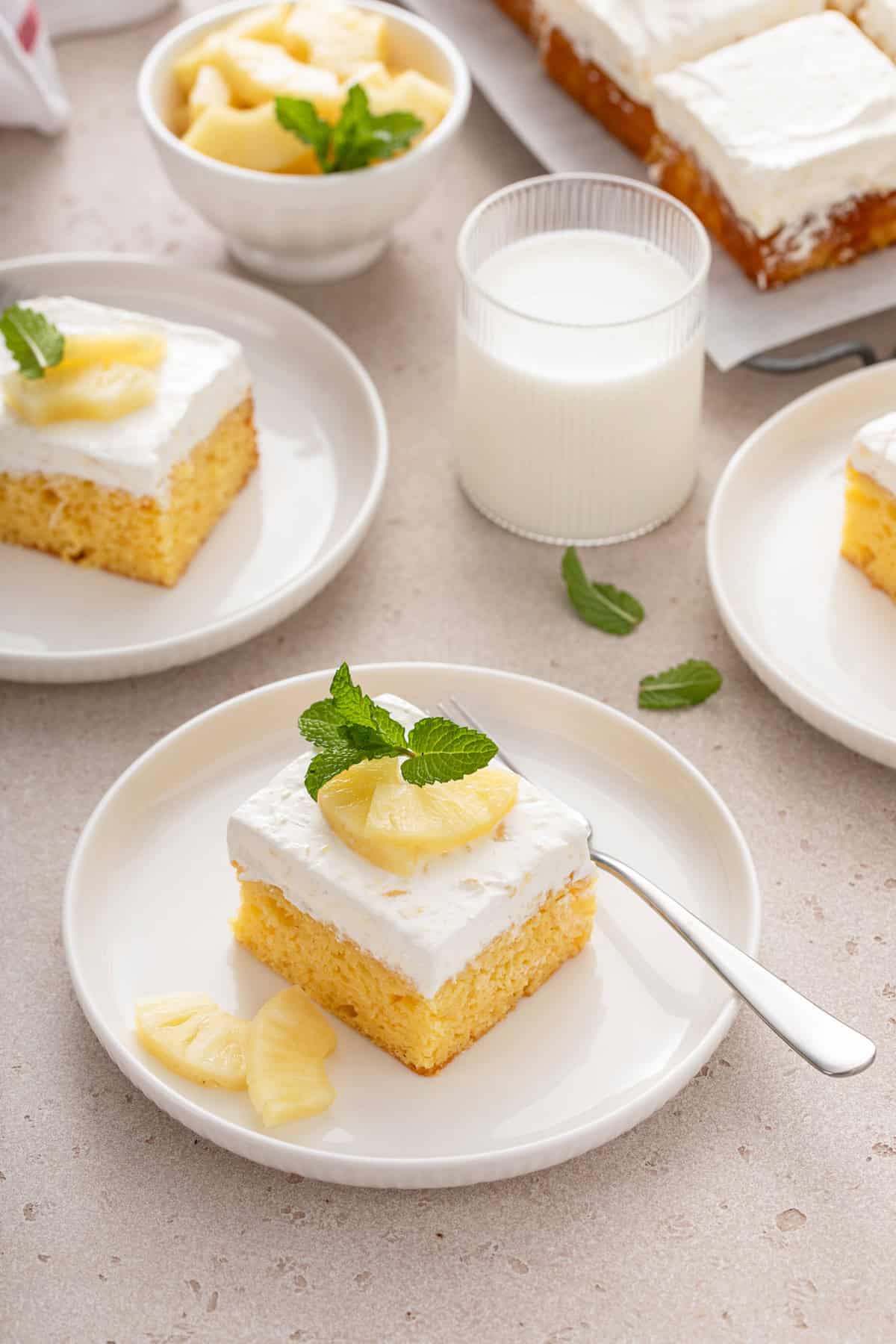 Several plated slices of easy pineapple cake around a glass of milk.