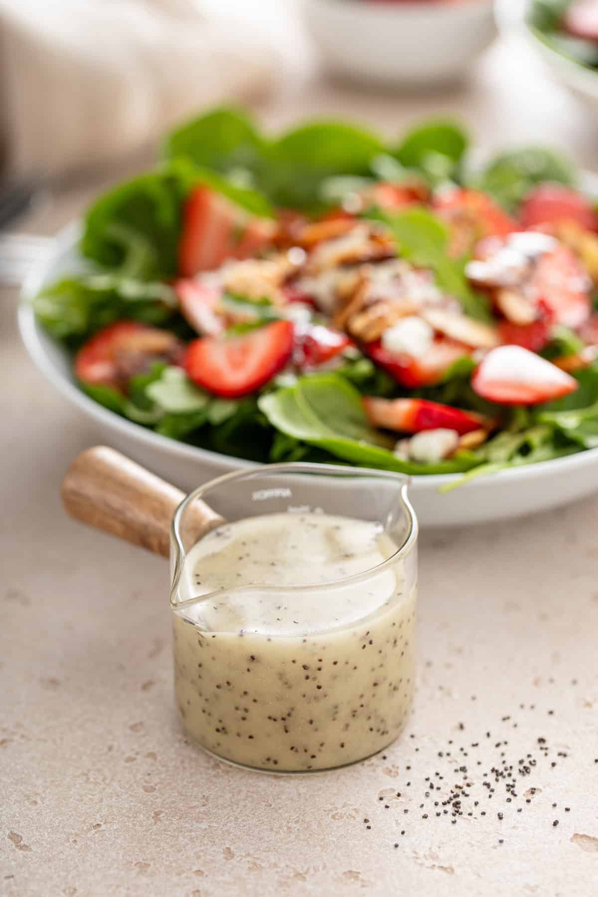 Jar of poppy seed dressing in front of a large bowl of strawberry spinach salad.
