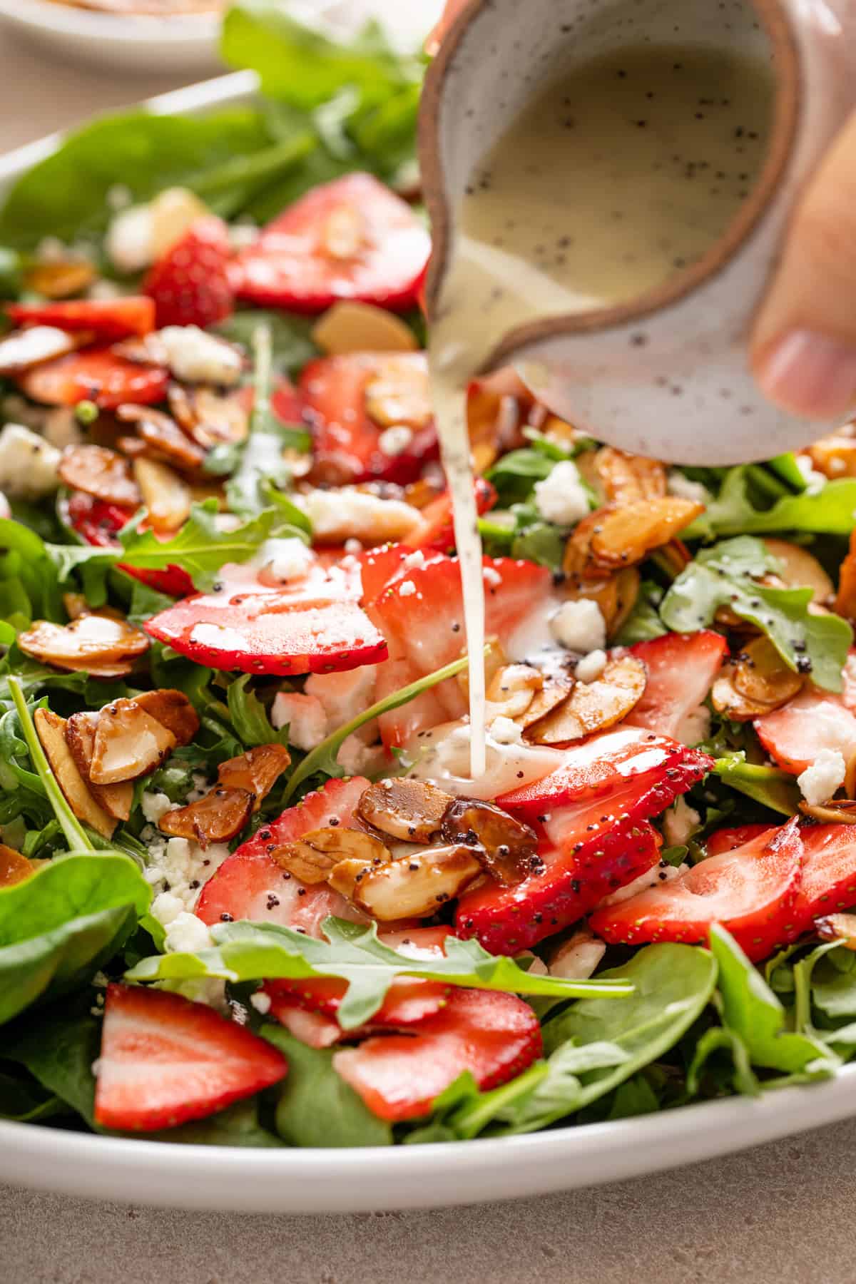 Poppy seed dressing being poured over the top of a strawberry spinach salad.
