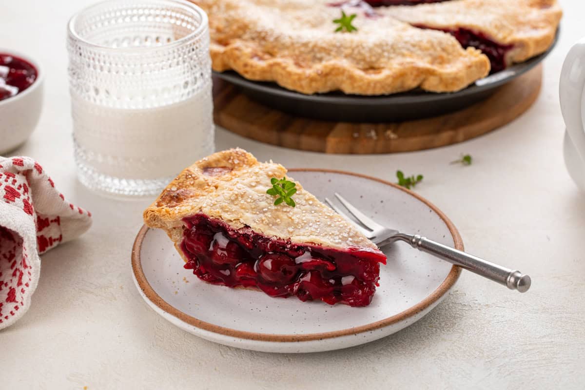 Slice of sour cherry pie next to a fork on a plate.