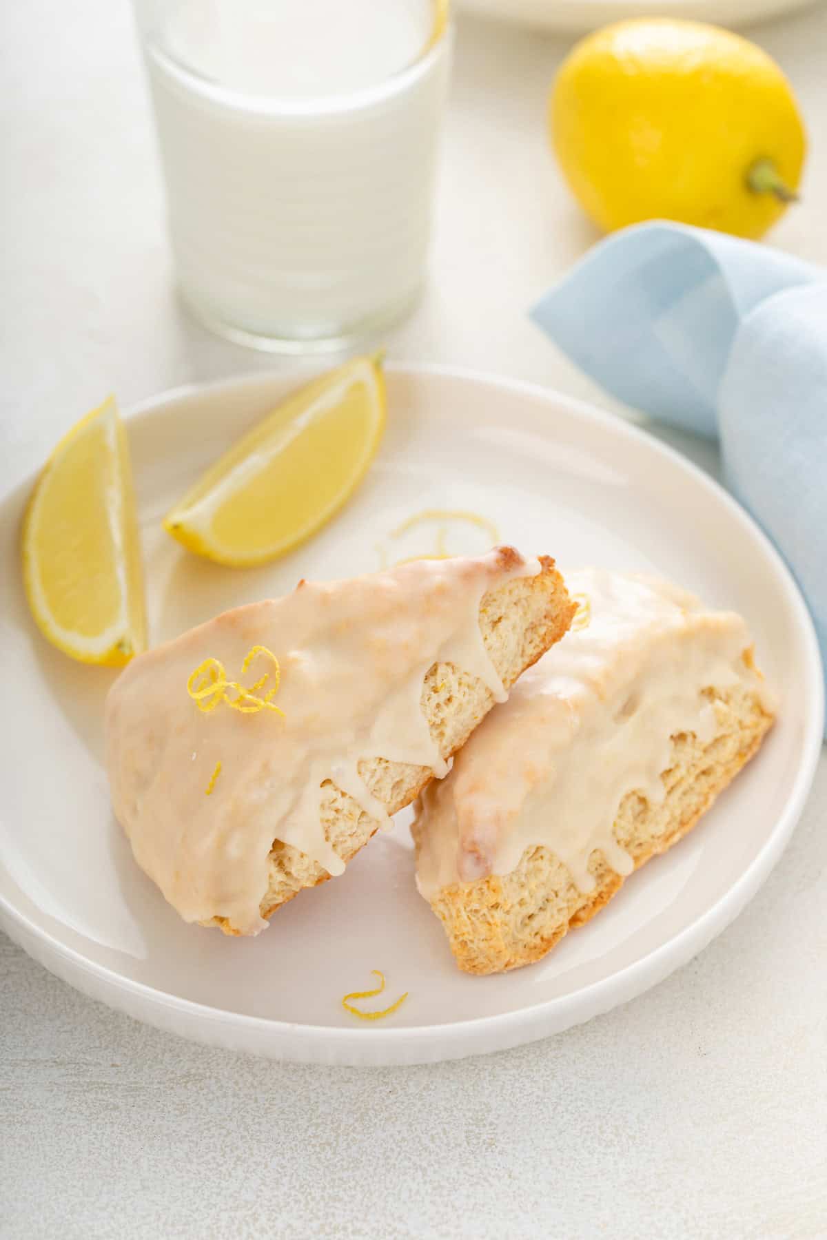 Two lemon scones next to lemon wedges on a white plate.