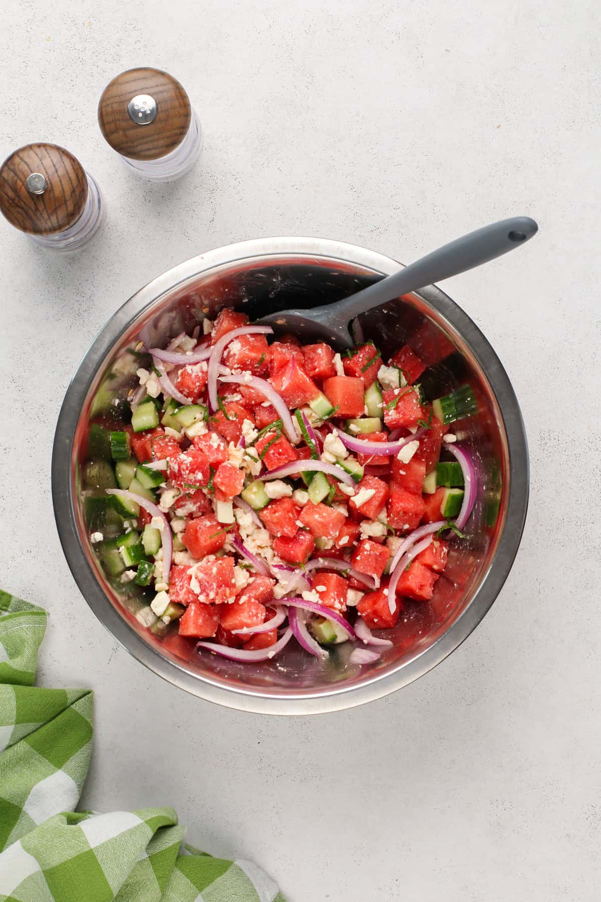 Watermelon feta salad being stirred together with a spatula in a metal bowl.