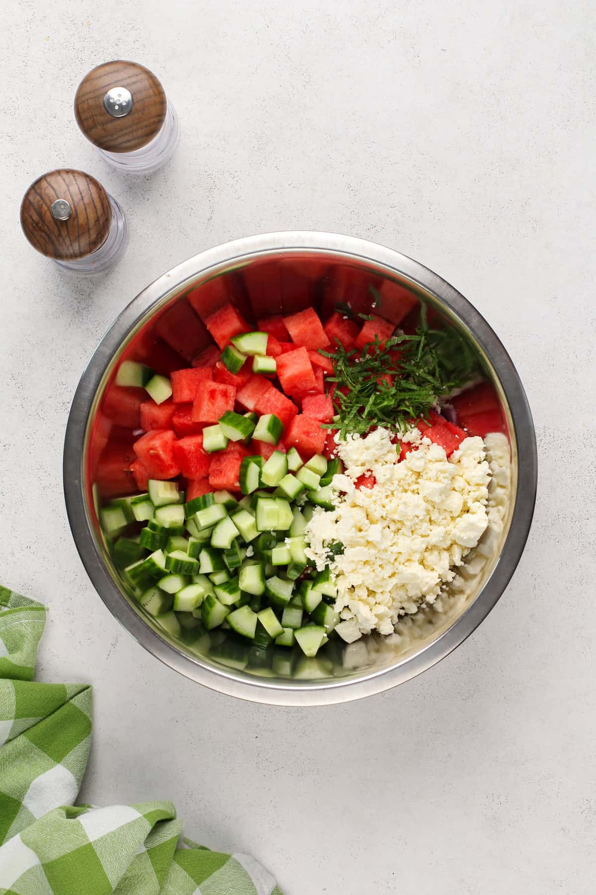 Ingredients for watermelon feta salad added to a metal bowl.