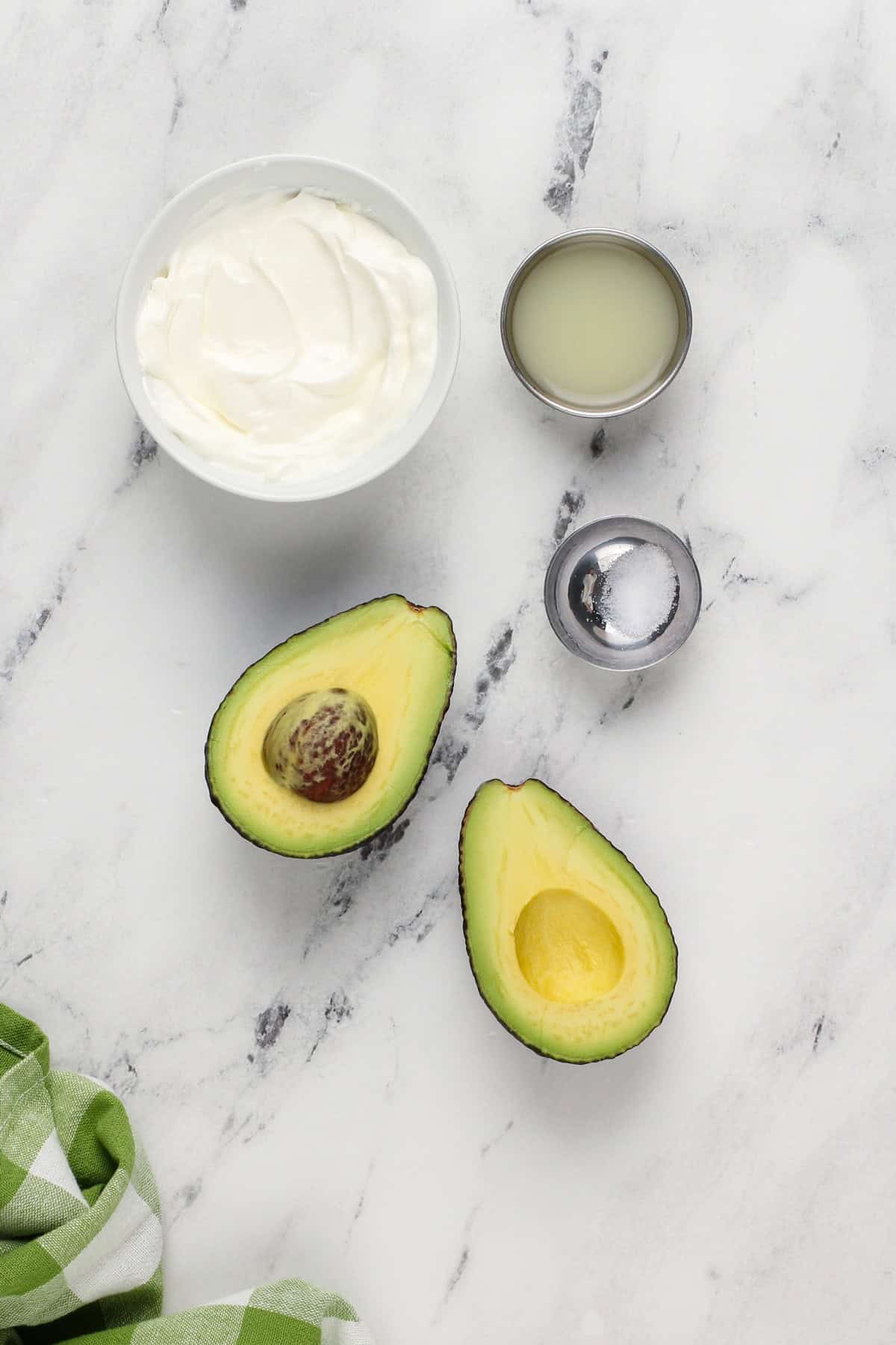 Ingredients for avocado crema arranged on a marble countertop.