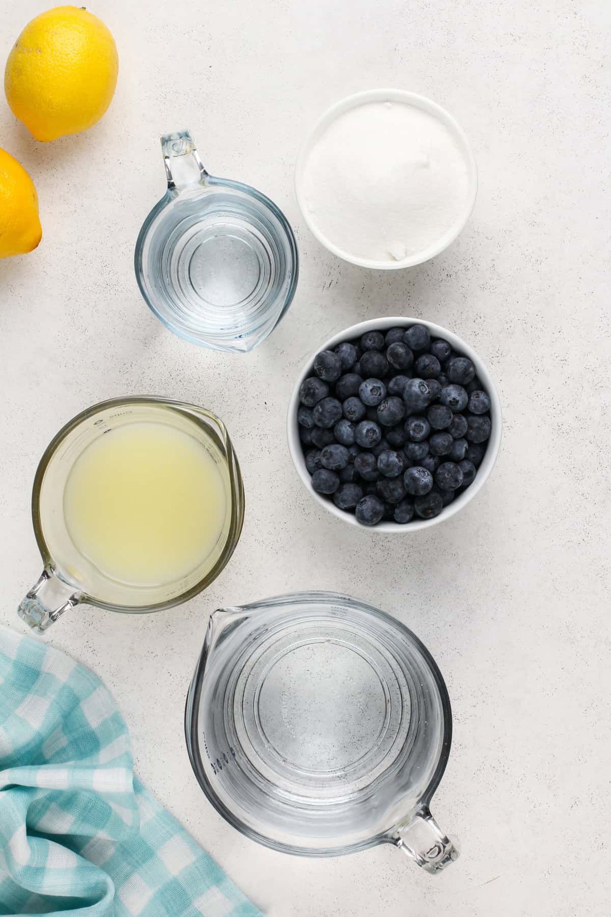 Ingredients for blueberry lemonade arranged on a light-colored countertop.