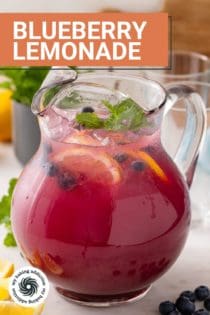 Glass pitcher filled with blueberry lemonade and garnished with lemon slices, fresh blueberries, and mint. Text overlay includes recipe name.
