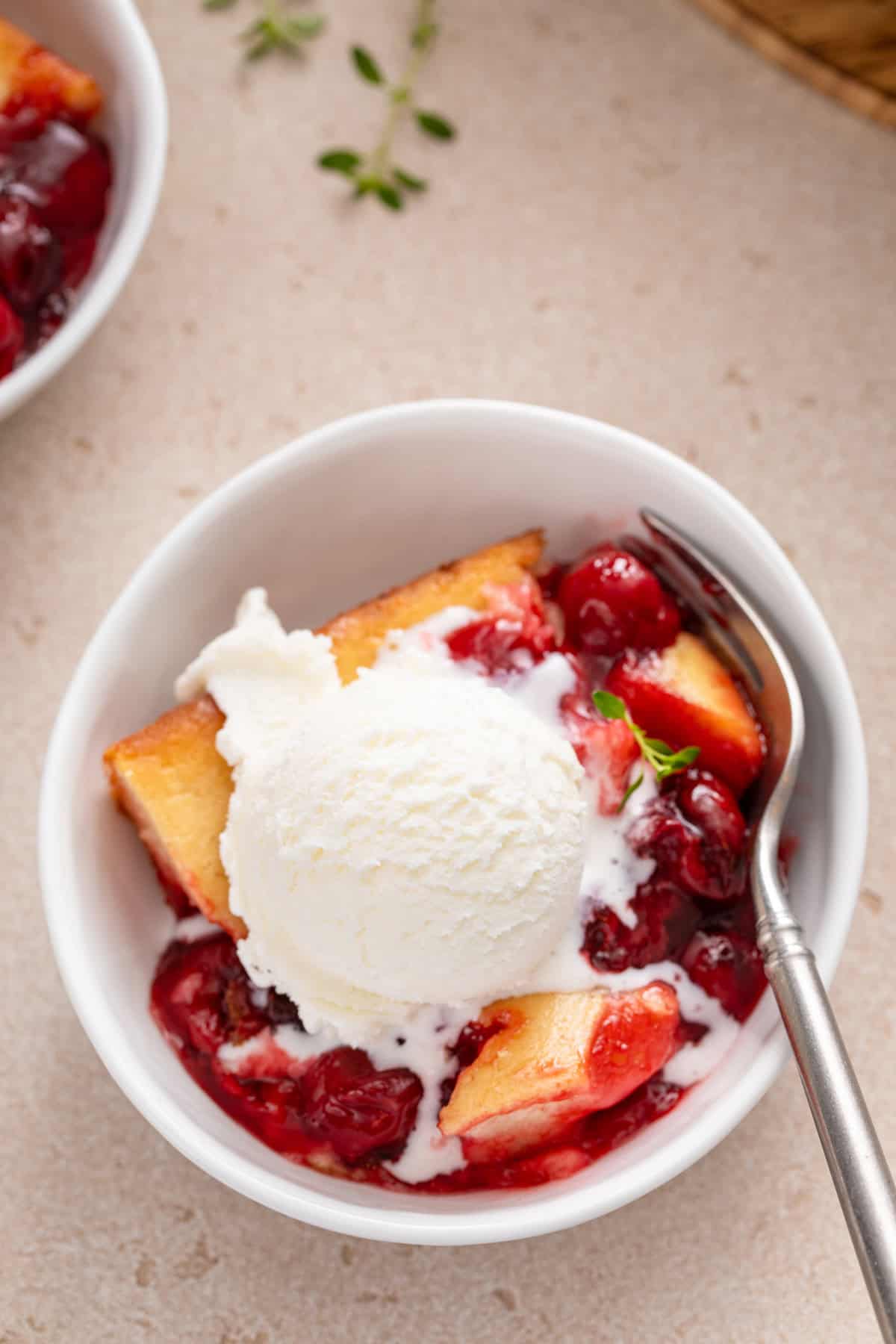 Overhead close up of a white bowl filled with a serving of easy cherry cobbler topped with ice cream.