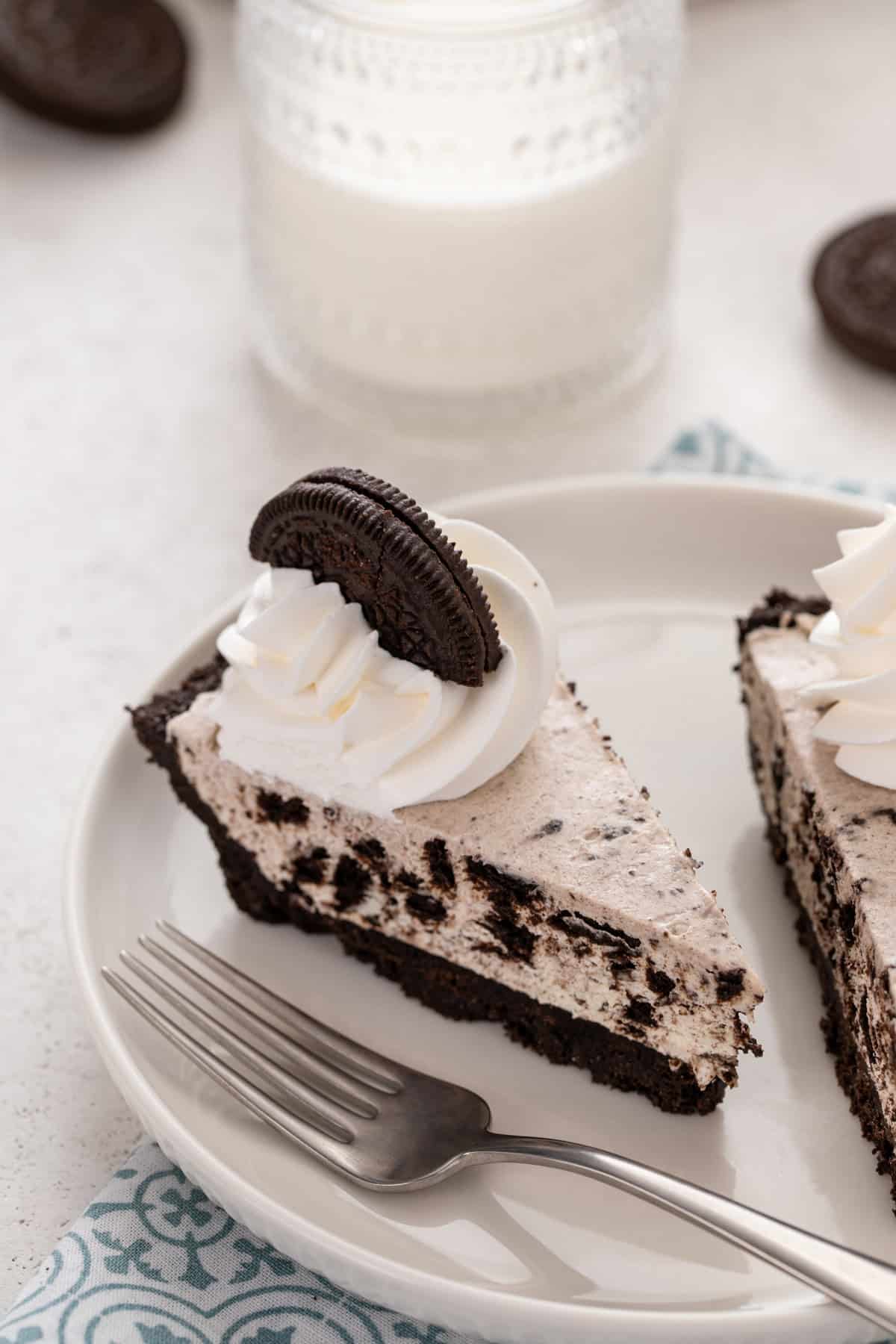 Close up of a slice of oreo pie topped with whipped cream and an oreo cookie on a white plate.