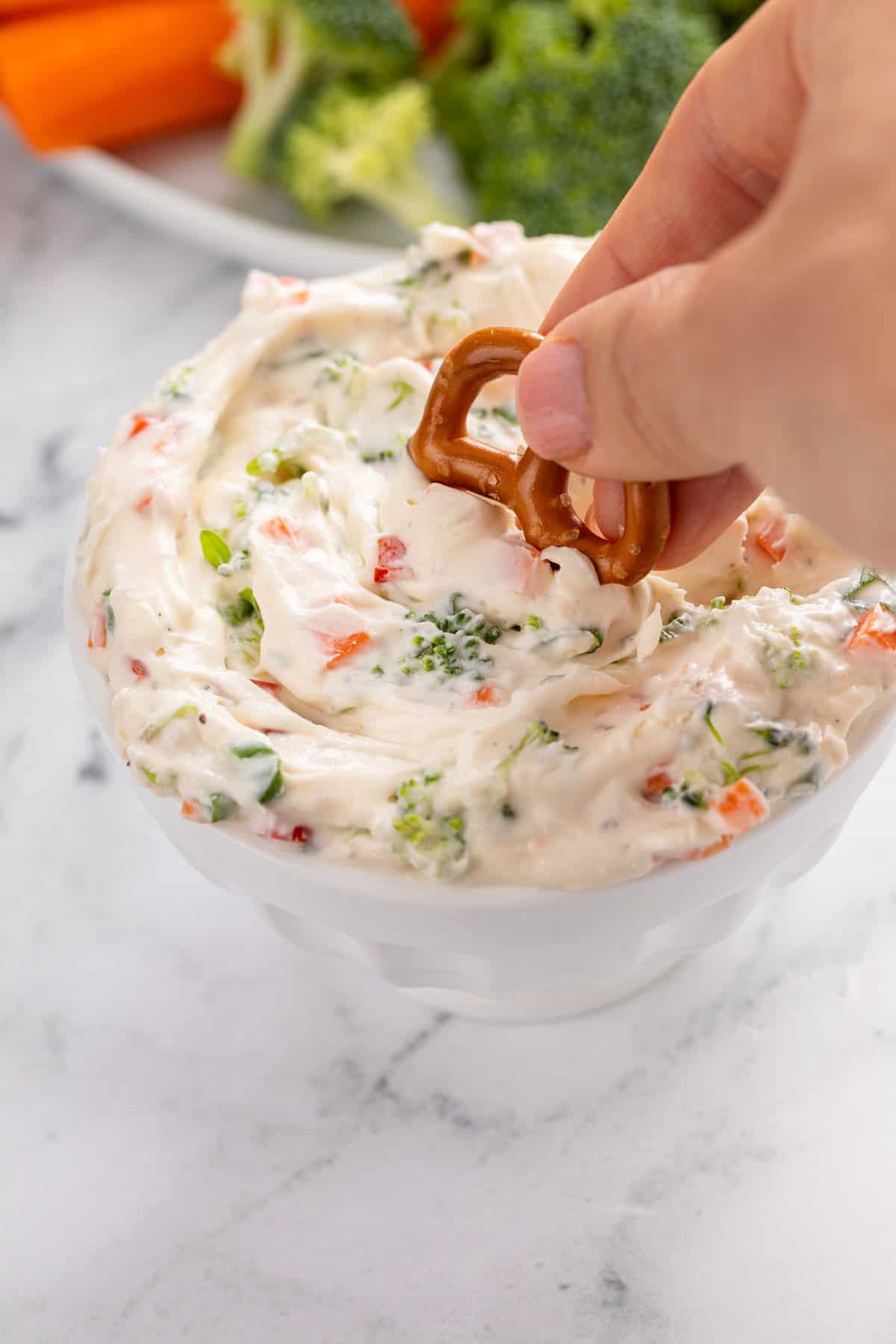 Hand dipping a pretzel twist into a bowl of veggie cream cheese.