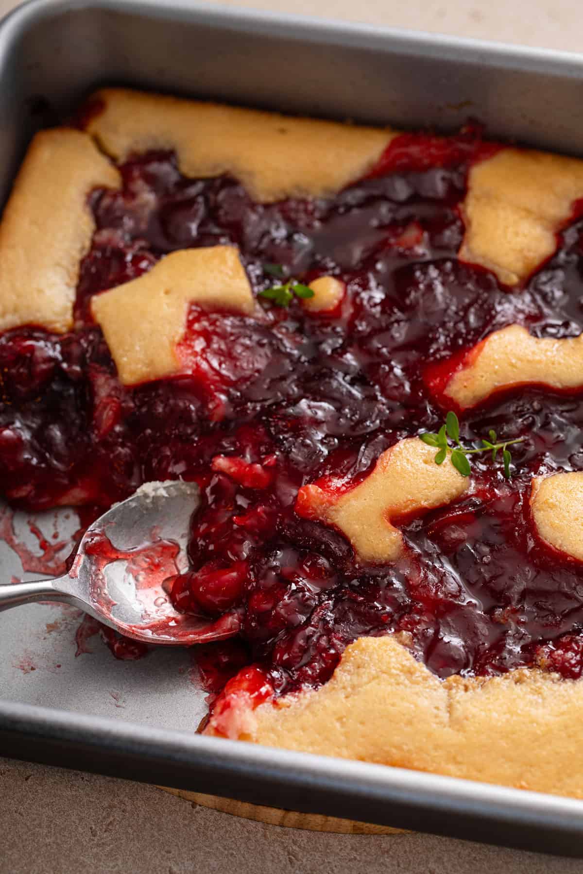 Close up of a serving spoon in a pan of easy cherry cobbler.