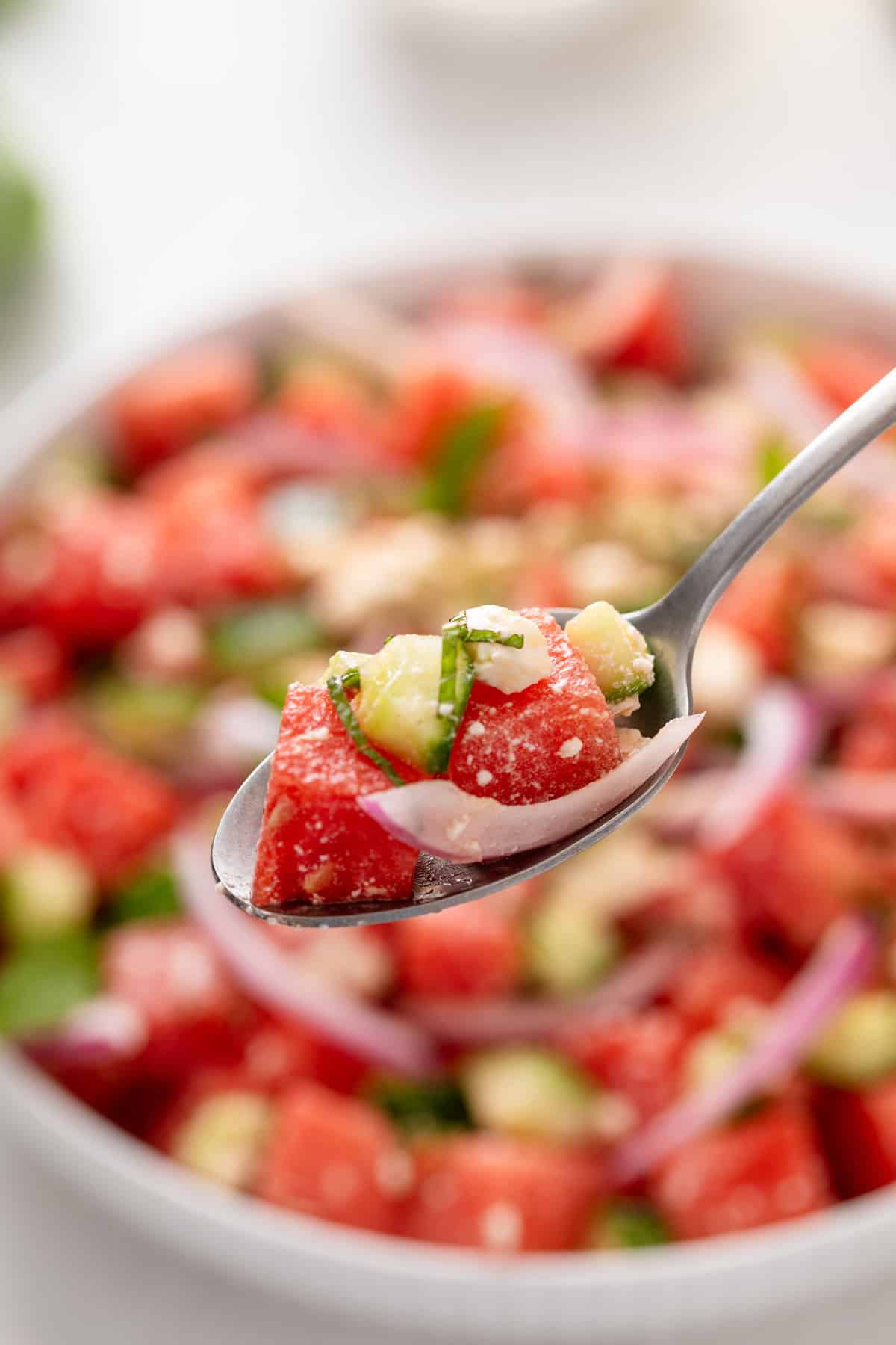 Spoon holding up a bite of watermelon feta salad.