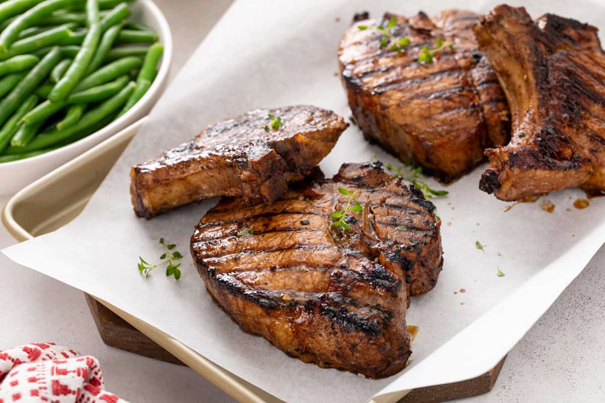 Four grilled pork chops resting on a parchment-lined sheet pan.