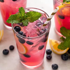 Glass of blueberry lemonade garnished with mint and fresh blueberries.