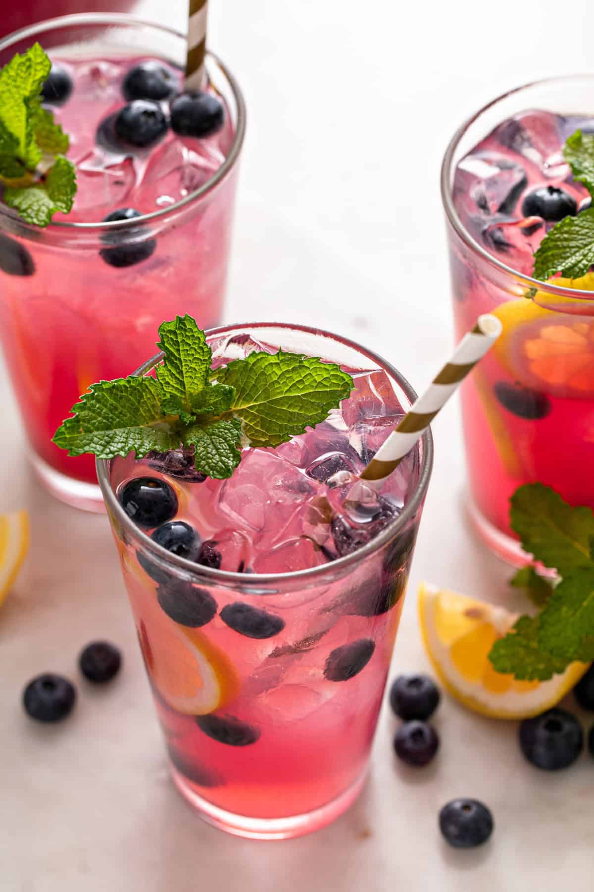 Glasses of blueberry lemonade garnished with mint, blueberries, and lemon slices.