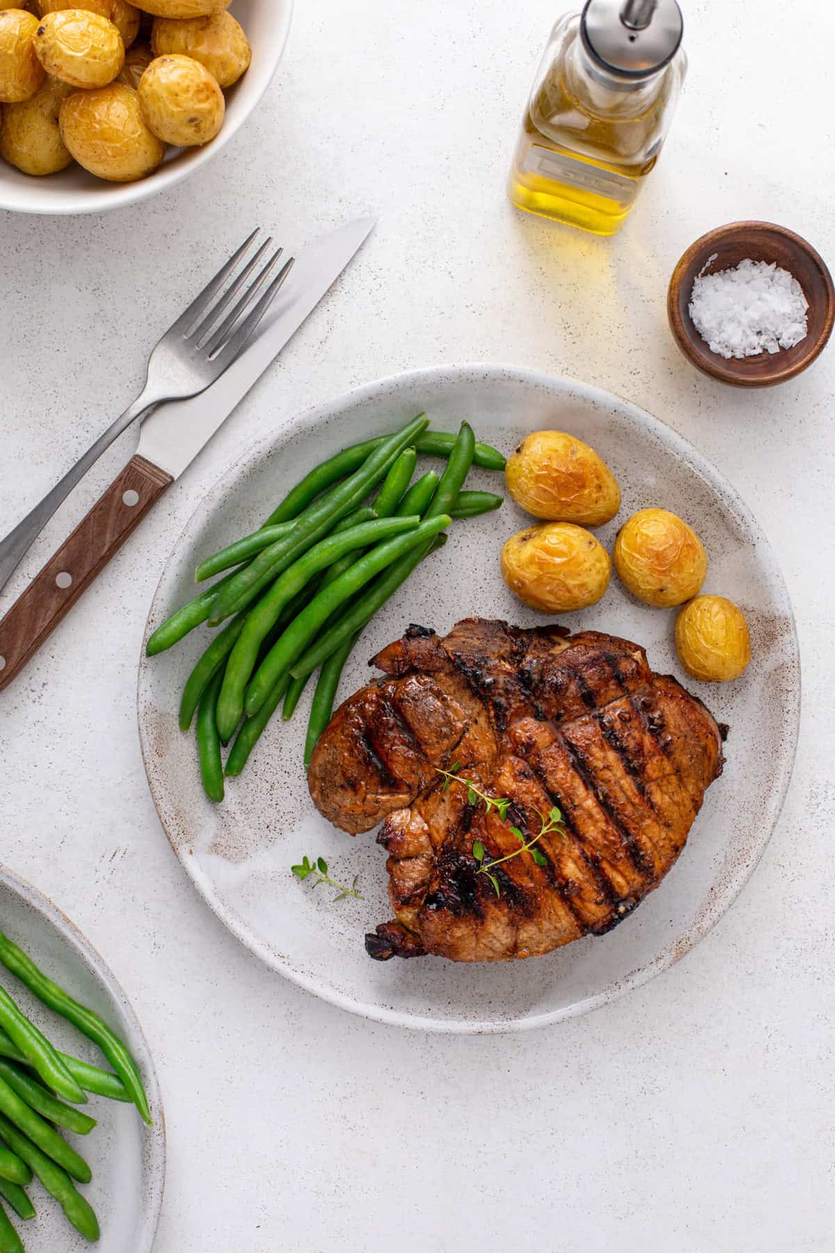 Overhead view of a grilled pork chop plated next to potatoes and green beans.