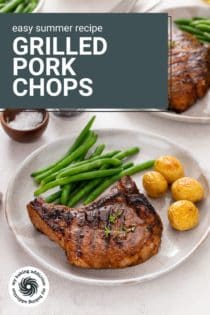Grilled pork chop on a plate next to roasted potatoes and green beans. A second plate is visible in the background. Text overlay includes recipe name.