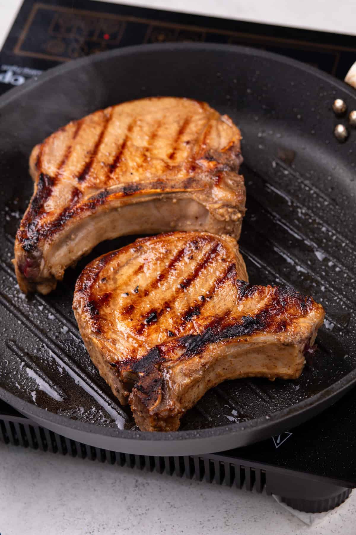 Two pork chops cooking on a grill pan.
