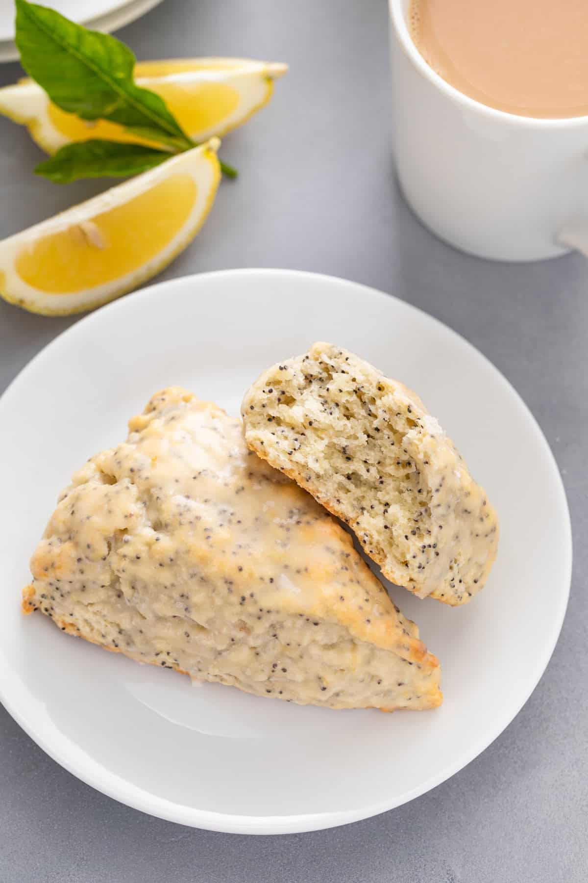 Halved lemon poppy seed scone propped against a whole scone on a white plate.