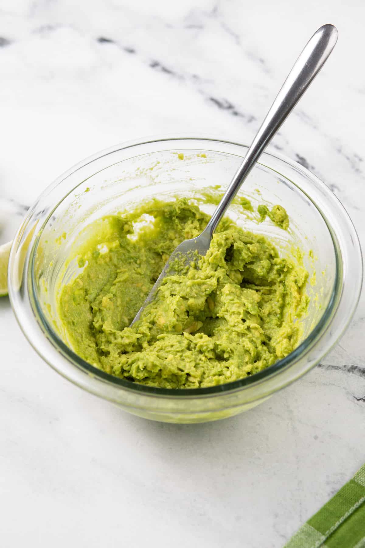 Mashed avocado in a glass bowl.