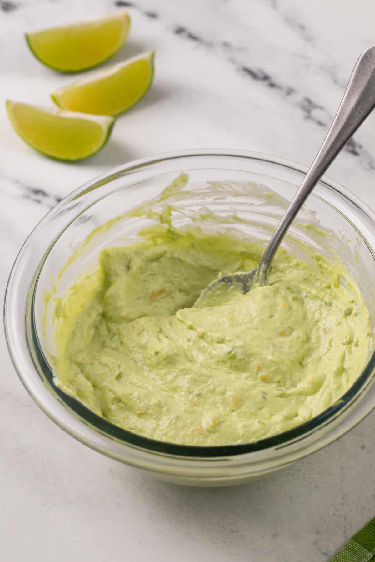 Avocado crema being stirred together in a glass bowl.