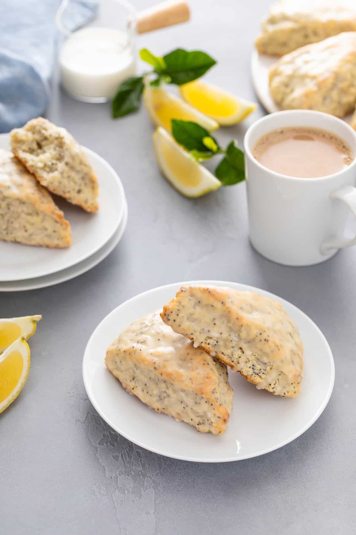 Two plates with lemon poppy seed scones in front of a cup of coffee.