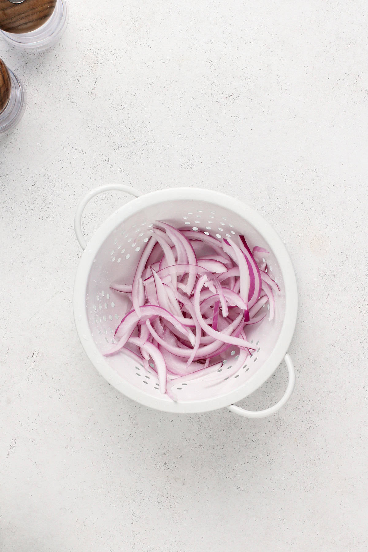 Sliced red onion rinsed with water in a white colander.
