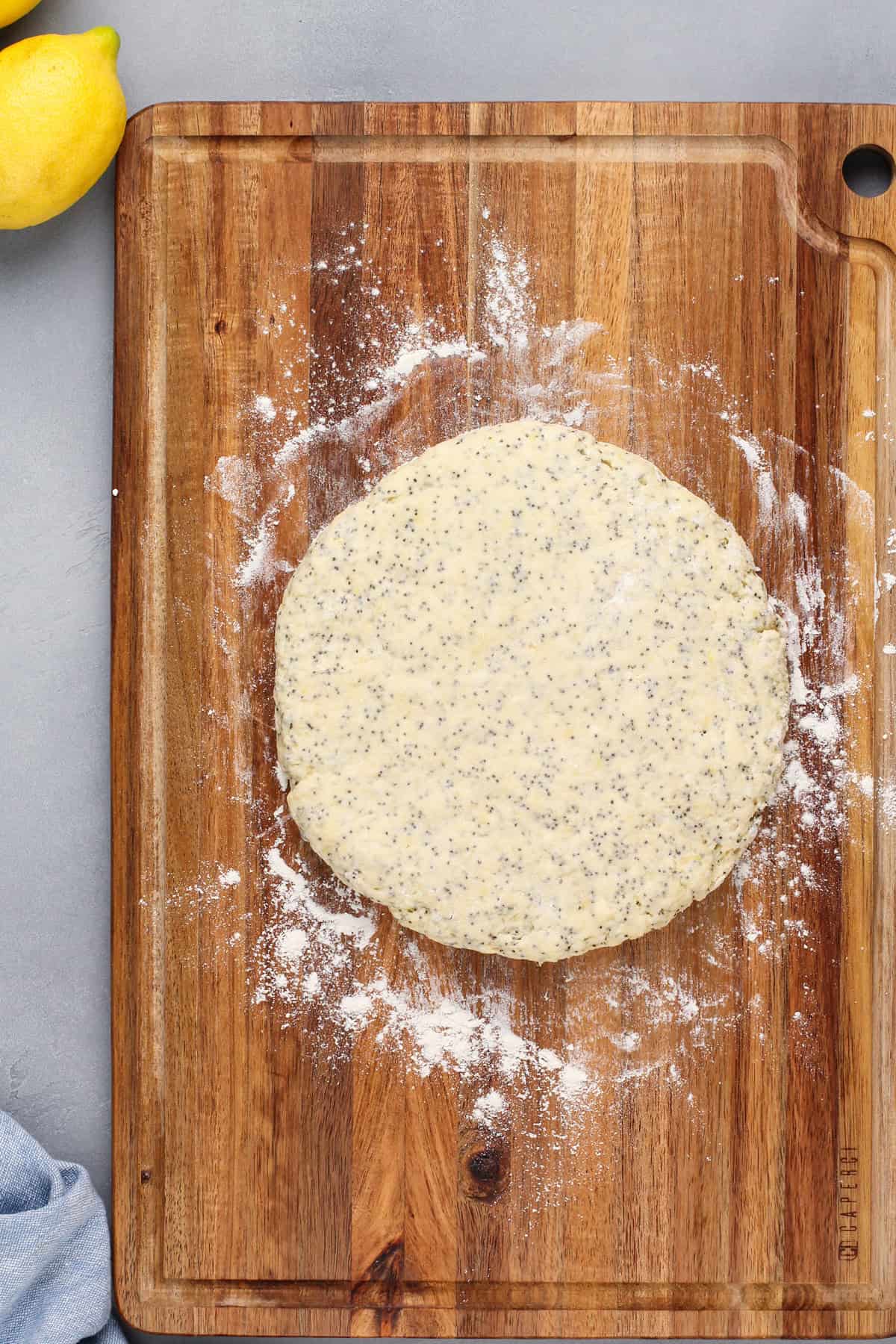 Lemon poppy seed scone dough shaped into a disk on a floured cutting board.