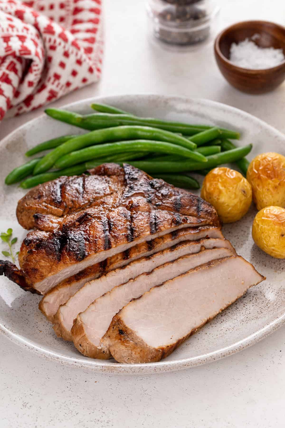 Sliced grilled pork chop on a plate next to roasted potatoes and green beans.