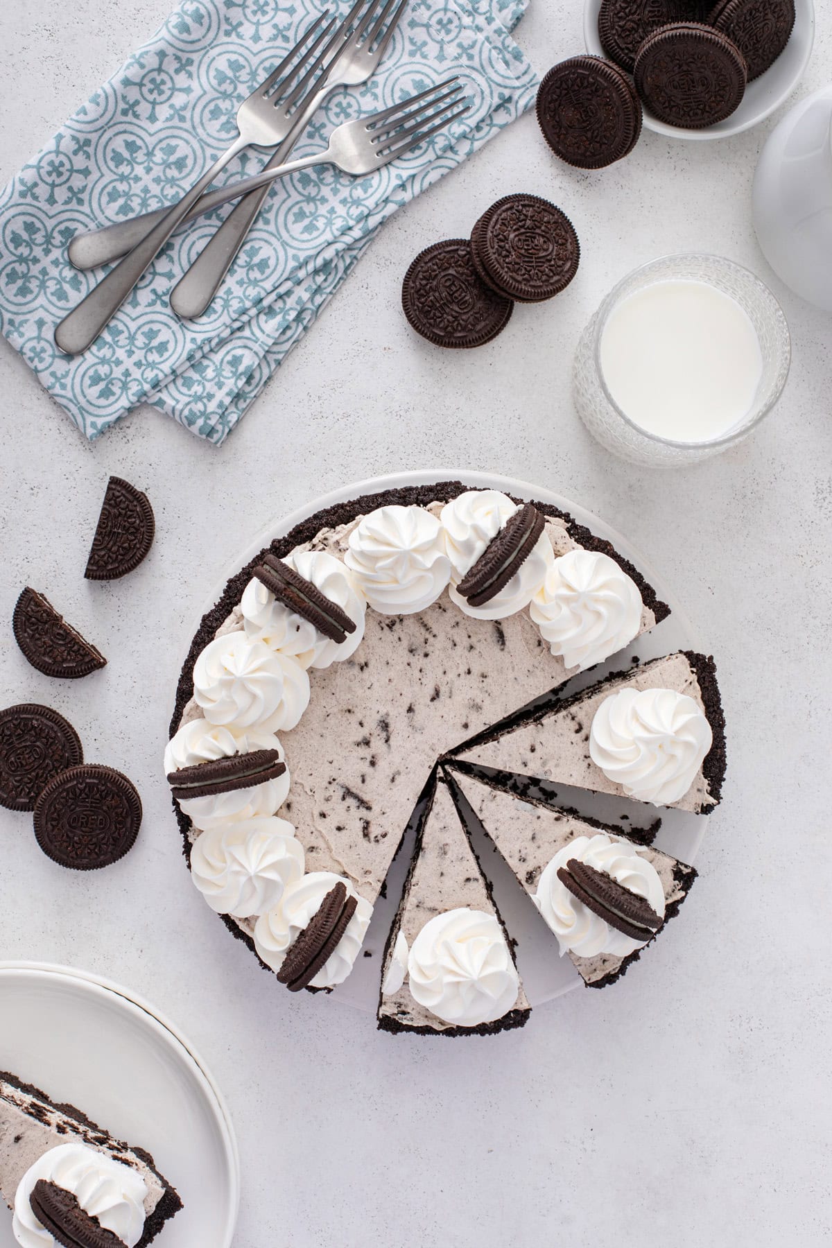 Overhead view of a sliced oreo pie on a countertop next to a glass of milk and oreo cookies.