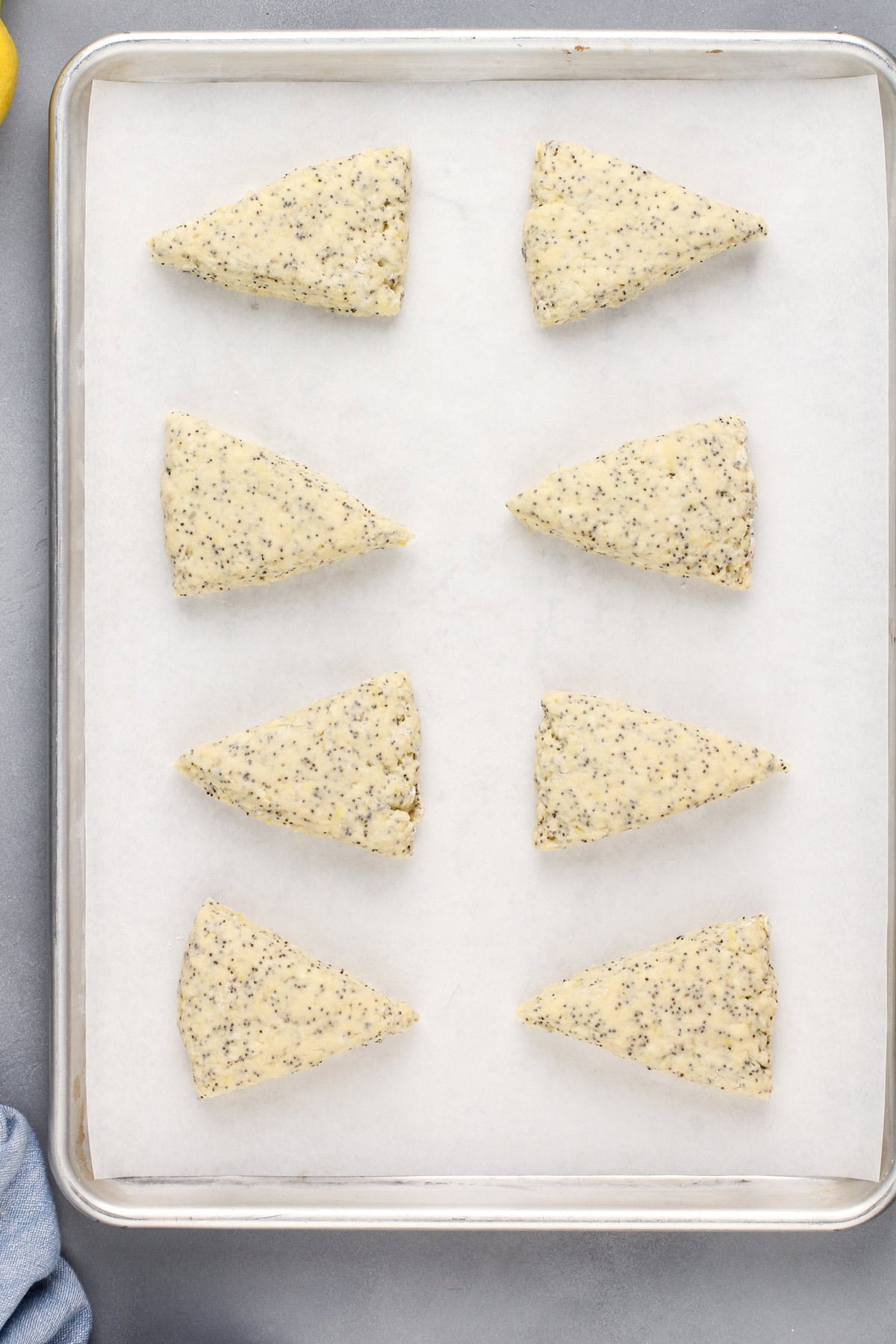 Unbaked lemon poppy seed scones on a lined baking sheet, ready to go in the oven.