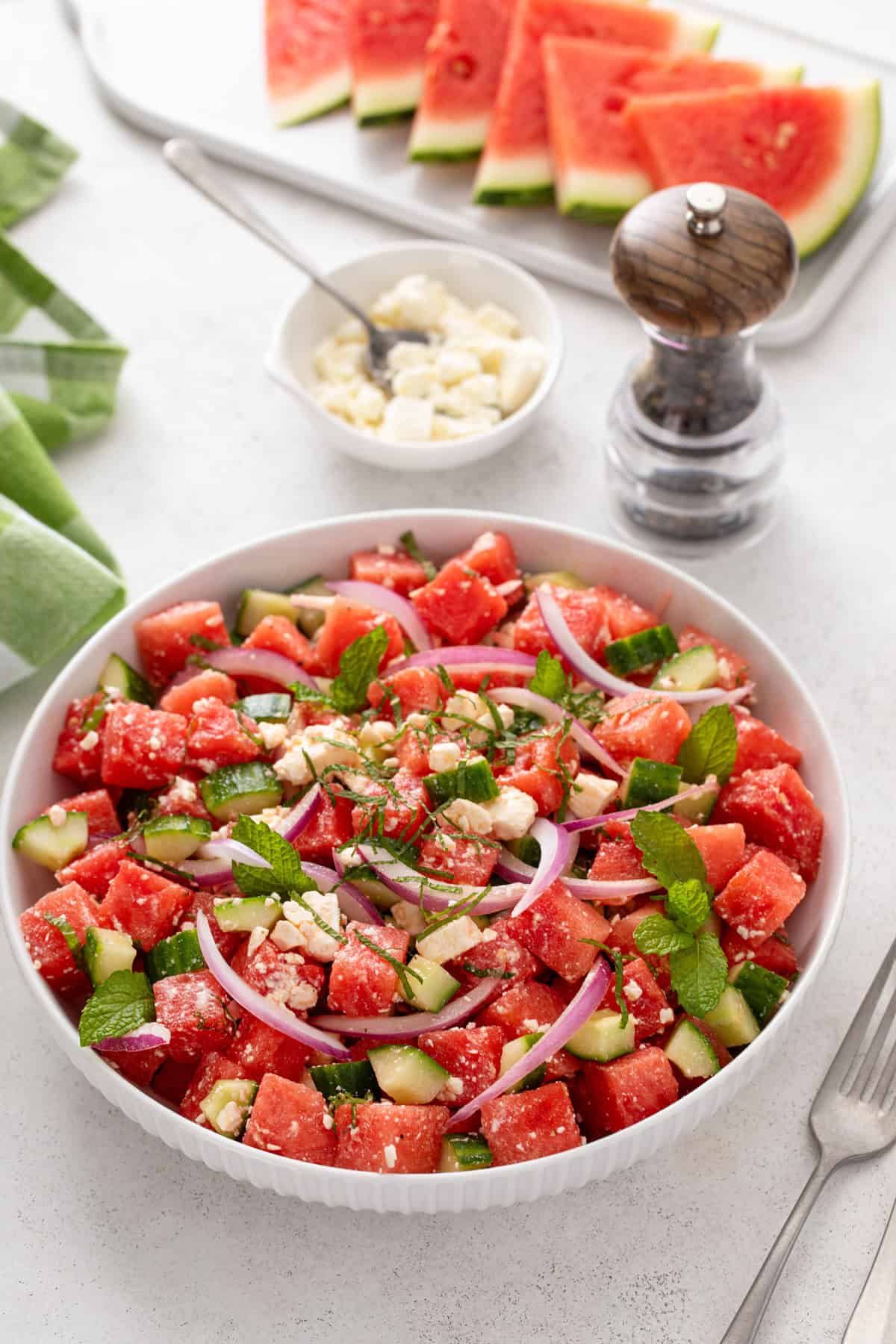 White serving bowl filled with watermelon feta salad with slices of watermelon in the background.