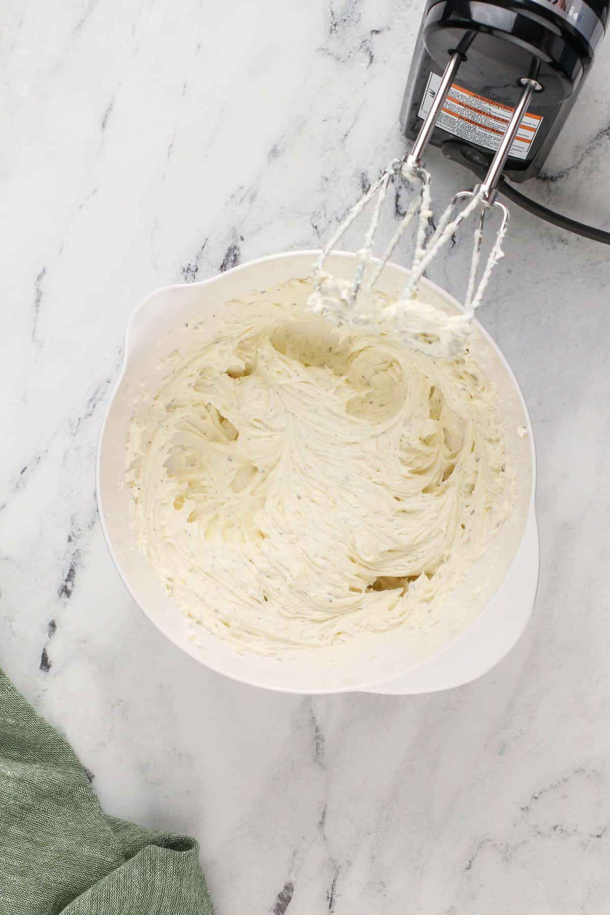 Cream cheese whipped with a mixer in a white bowl.