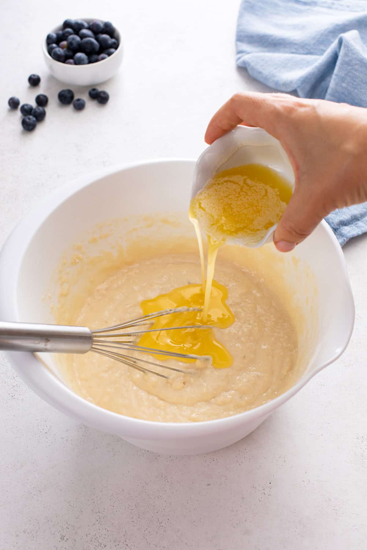 Melted butter being poured into pancake batter in a white bowl.
