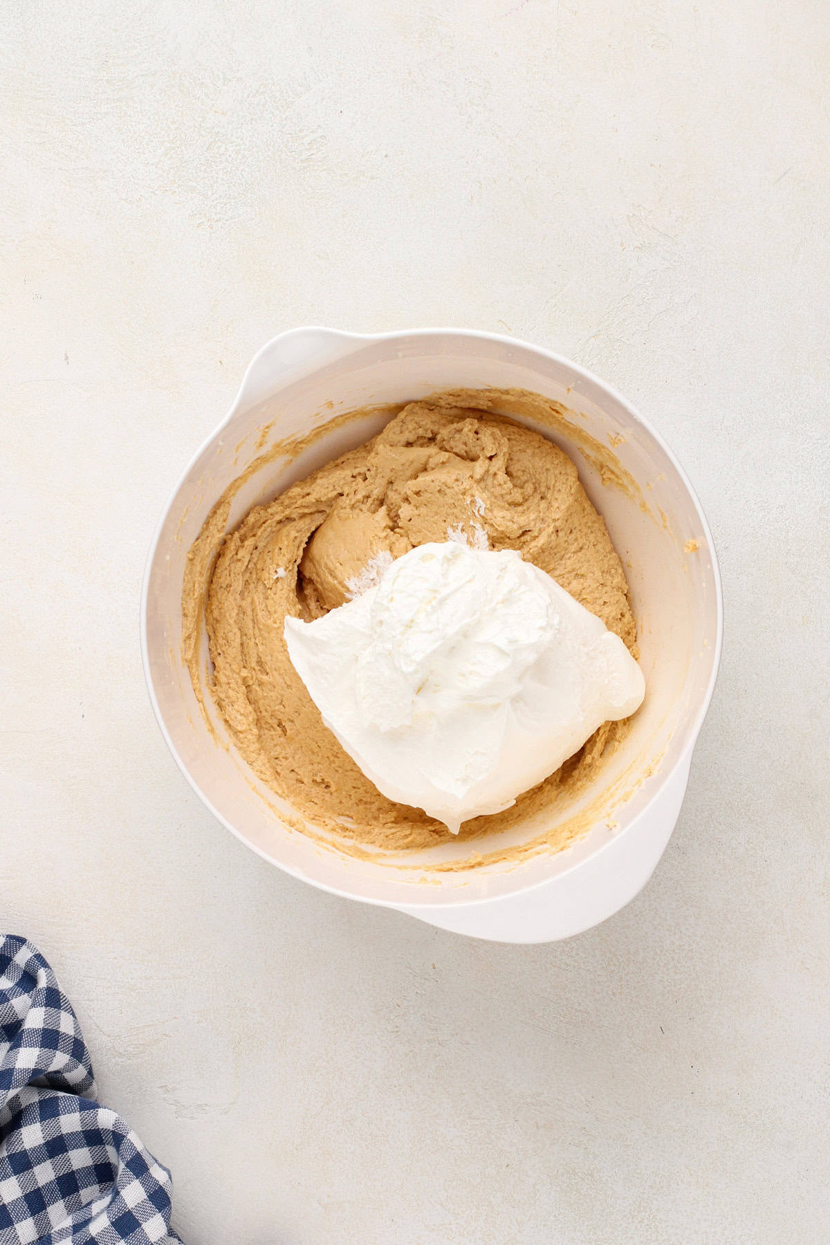 Cool whip being added to peanut butter dip in a white bowl.