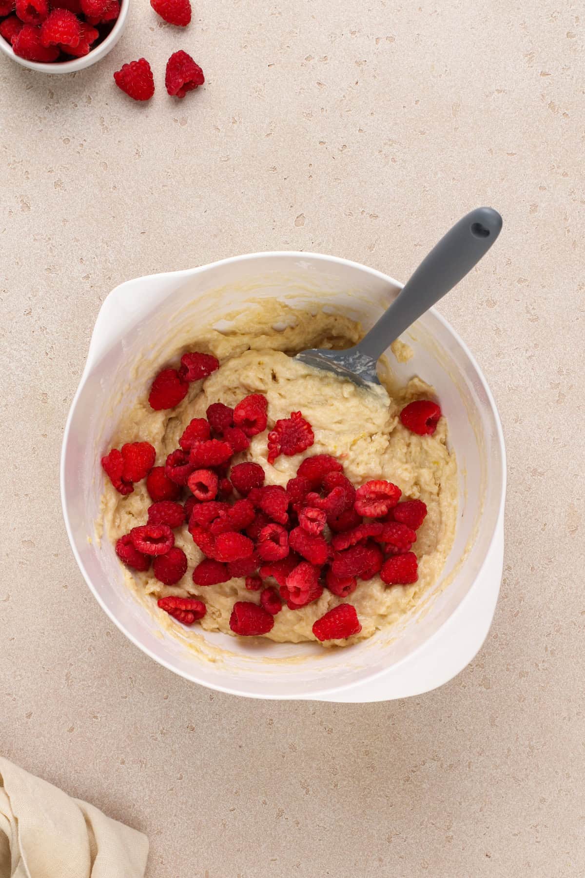 Fresh raspberries being added to muffin batter in a white bowl.