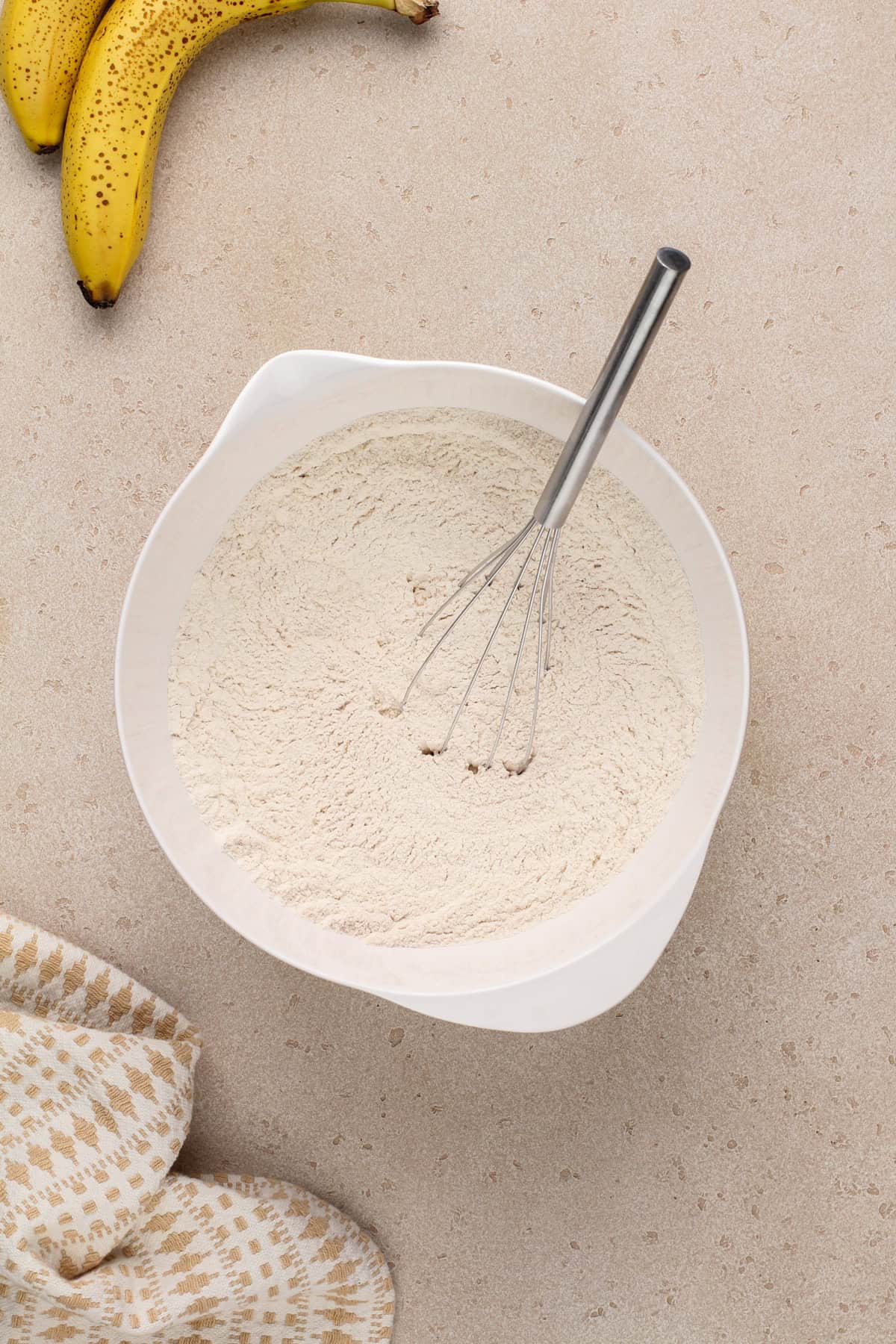 Dry ingredients for banana bread muffins whisked together in a white mixing bowl.