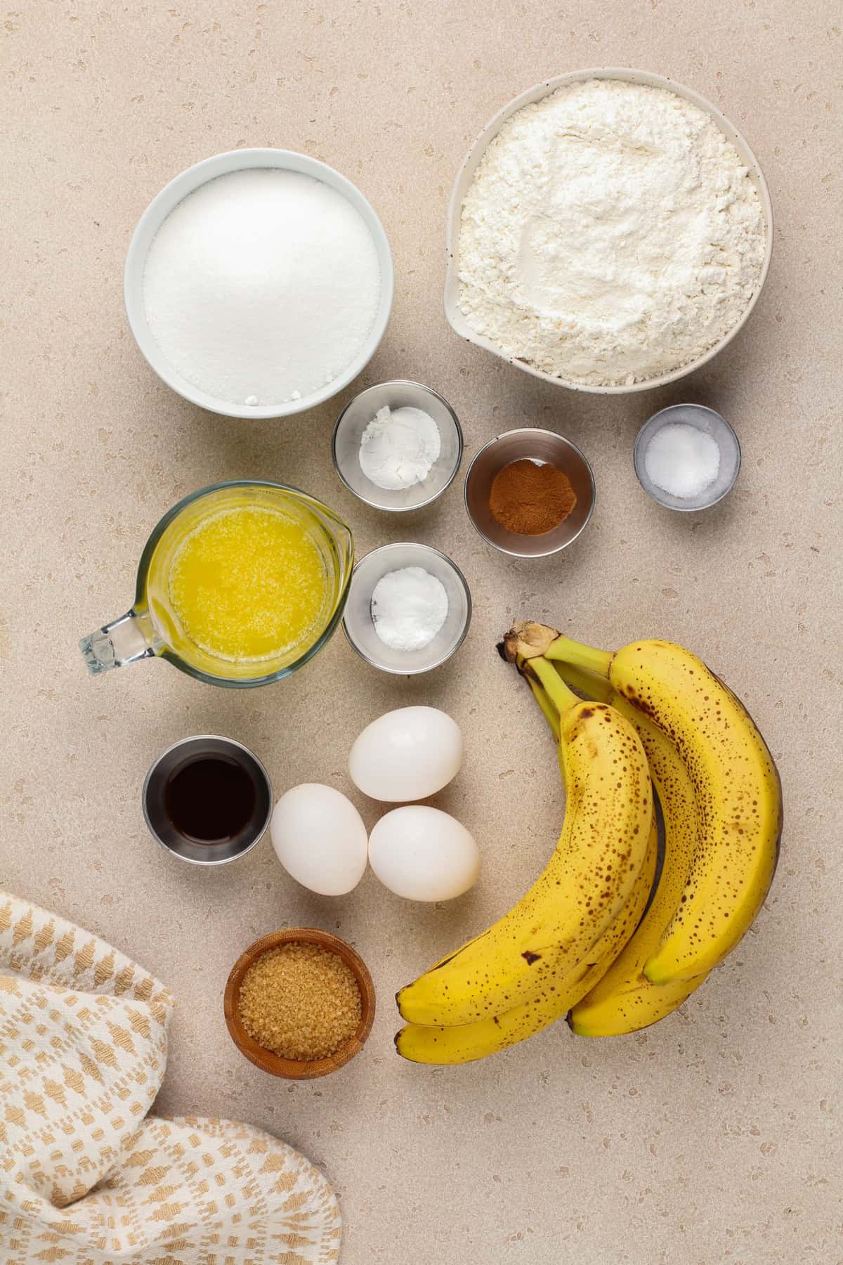 Ingredients for banana bread muffins arranged on a beige countertop.