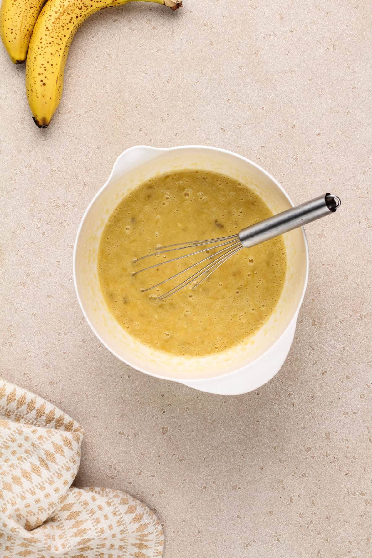 Wet ingredients for banana bread muffins whisked together in a white bowl.