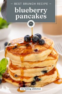 Syrup being poured over a stack of blueberry pancakes on a white plate. Text overlay includes recipe name.