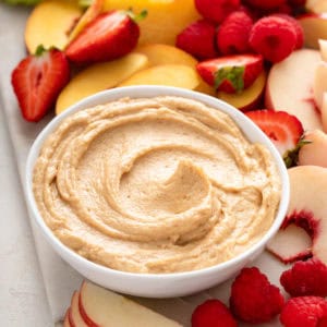 Bowl of peanut butter dip surrounded by fresh fruit.