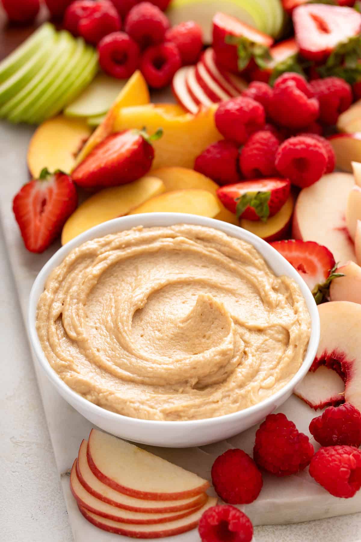 White bowl of peanut butter dip set on a platter of fresh fruit.