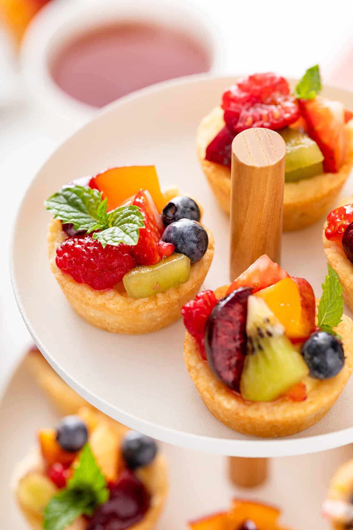 Close up of 3 mini fruit tarts at the top of a tiered dessert plate.