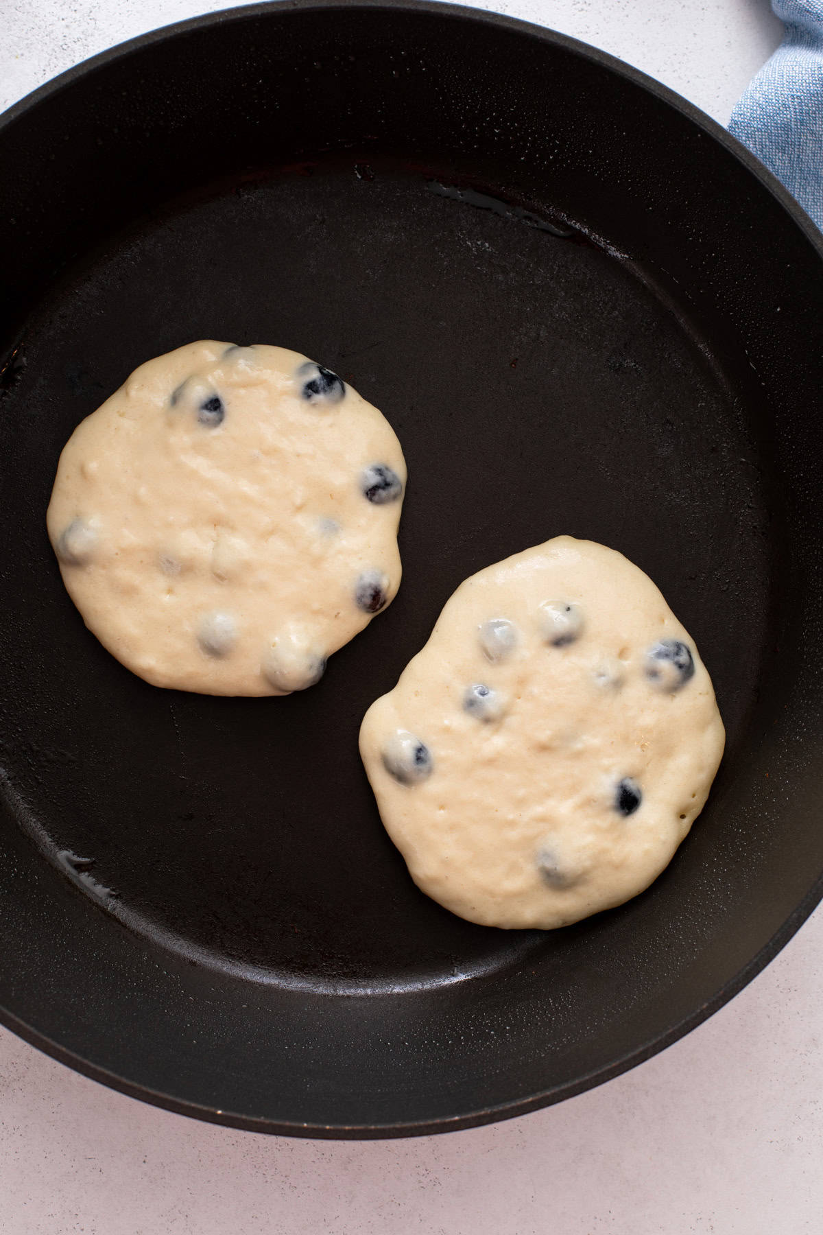 Two blueberry pancakes cooking in a black skillet.
